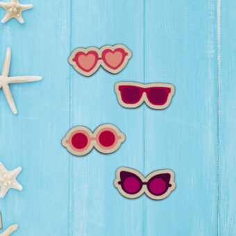 Petites broches en bois en forme de lunettes de différents styles et imprimées dans les couleurs de rose et de violet vifs.